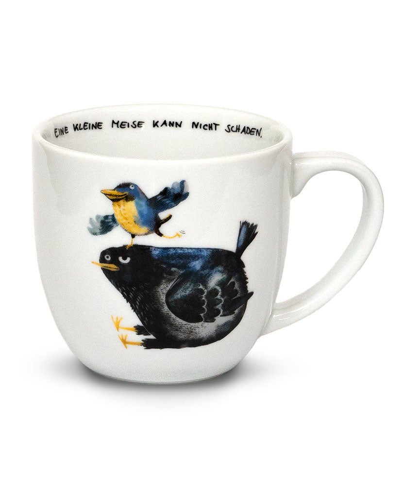 Weiße bauchige Tasse mit einer dicken Amsel drauf, auf dem Kopf von der Amsel tänzelt eine kleine Meise. Im Inneren der Tasse steht der Spruch: "Eine kleine Meise kann nicht schaden."