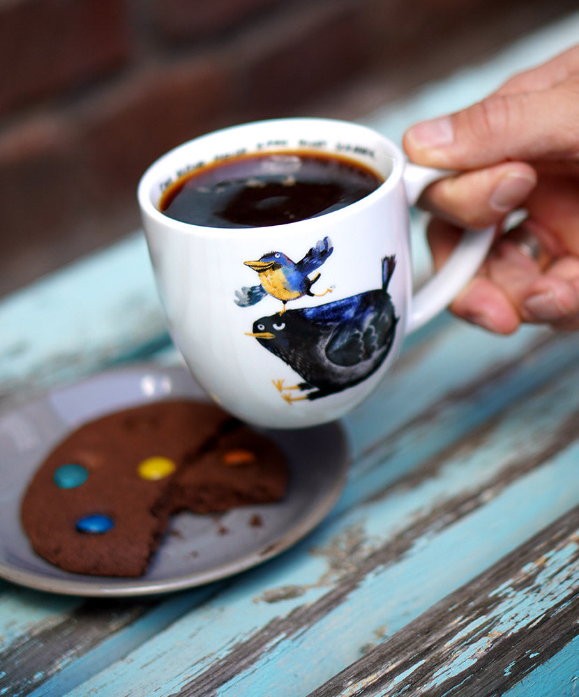 Tasse mit zwei Vögeln drauf gefüllt mit einem Kaffee.